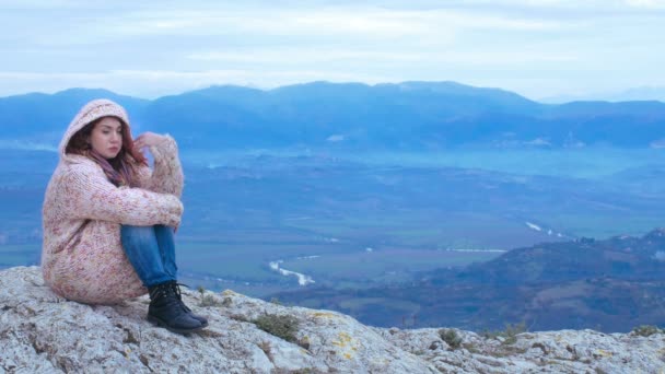 Joven pelirroja en un contexto natural sentada sobre roca, meditación, viento, frío — Vídeos de Stock