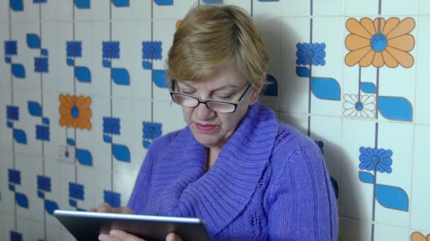 Elderly woman in the kitchen using tablet computer — Stock Video