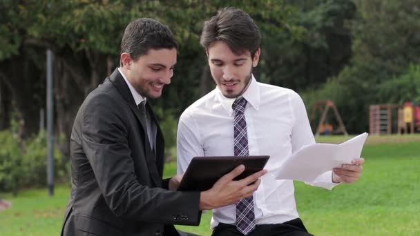Δύο επιχειρηματίες με υπολογιστή tablet μιλάμε για ένα έργο σε ένα πάρκο — Αρχείο Βίντεο