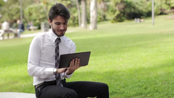 Feliz hombre joven de negocios utilizando tableta PC fuera en un parque — Vídeos de Stock