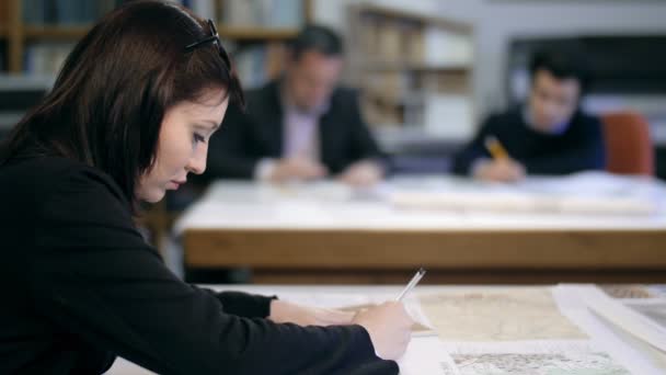 Diseñadora femenina en primer plano trabajando en planos: colegas en segundo plano — Vídeo de stock