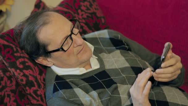 Yetişkin adam kanepede rahatlatıcı ve seyir onun akıllı telefon — Stok video