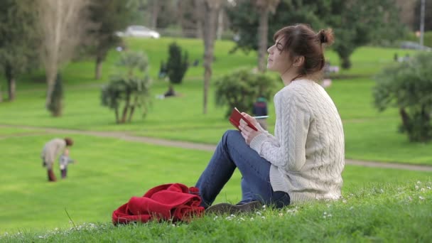 Bela jovem está escrevendo um diário ao ar livre no parque : — Vídeo de Stock