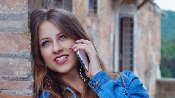 Улыбающийся подросток разговаривает по телефону: молодая женщина имеет телефонный звонок — стоковое видео