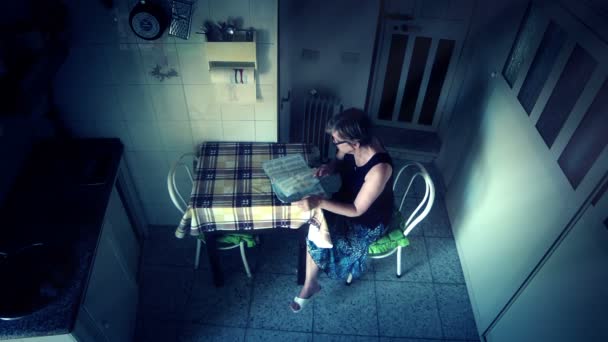 Ledsen en ensam kvinna läsande tabloid i sitt kök. ensamhet, sorg — Stockvideo