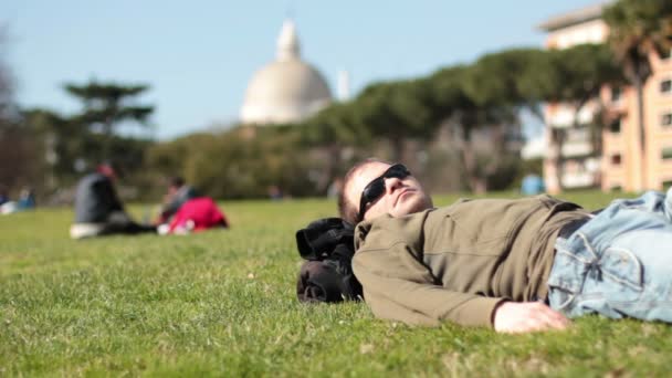 Man ligger på grönt gräs i en park avkopplande — Stockvideo