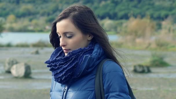 Depressief en doordachte jonge vrouw staat alleen in de buurt van een meer in een koude dag — Stockvideo