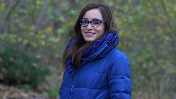Χαμογελαστά νεαρή γυναίκα στο πάρκο σε μια θυελλώδη κρύα χειμερινή ημέρα: αργή κίνηση μήκος σε πόδηα — Αρχείο Βίντεο