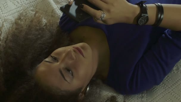 Bela mulher encaracolado deitado na cama está usando smartphone: telefone móvel — Vídeo de Stock