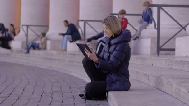 Молода жінка, за допомогою планшетного ПК, сидячи на сходах площі Святого Петра в Римі — стокове відео