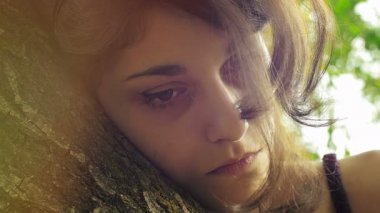 Ağaca yaslanmış oldukça güzel üzgün bir genç. 4K görüntüsünü kapat