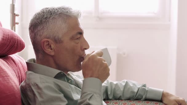 Homem bonito bebendo café quente no sofá vermelho: prazer, relaxante, relaxar, pausa — Vídeo de Stock