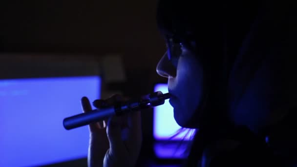 Hacker-Mädchen arbeitet am Computer und raucht elektronische Zigarette — Stockvideo