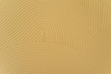 Close-up of a beige decorative plaster texture with curved lines and smooth grooves forming an abstract pattern. Minimalist surface background suitable for interior design, construction, or texture mockups.