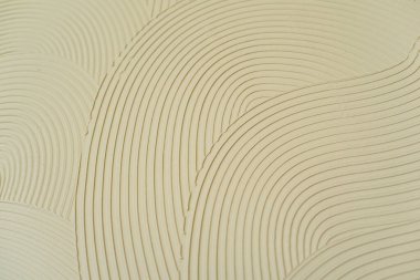 Close-up of a beige decorative plaster texture with curved lines and smooth grooves forming an abstract pattern. Minimalist surface background suitable for interior design, construction, or texture mockups.