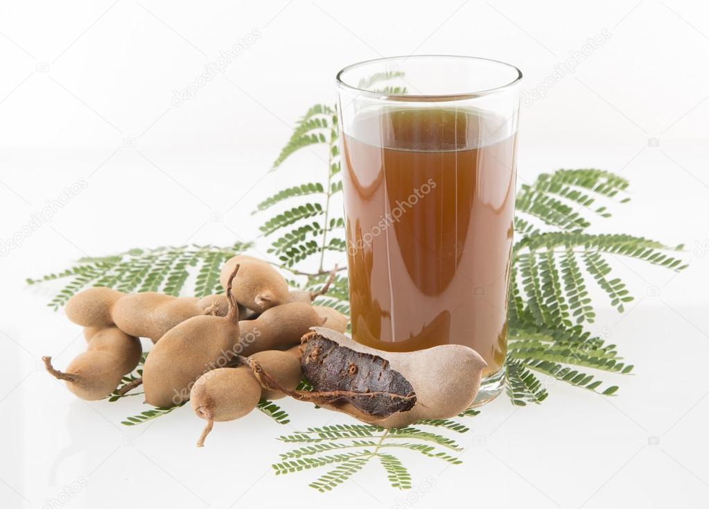Tamarind juice in a glass surrounded by fresh ripe tamarinds and tamarinds leaves