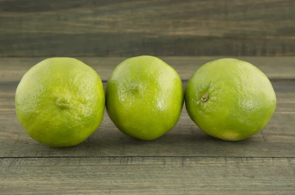 Green lemons on wooden table — Stock Photo, Image