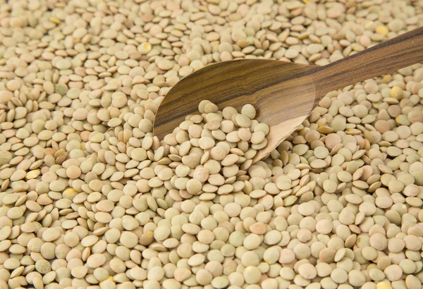 Scattered raw lentils and wooden spoon — Stock Photo, Image