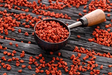 Bir kaşığa konmuş organik kırmızı notatto tohumları ve alta saçılmış Bixa orellana