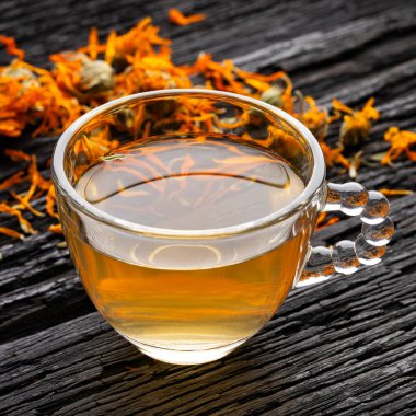 Calendula bitkisel karışım, kırsal bir arka planda, temiz bir cam bardakta servis edilir.