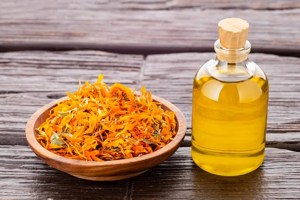 Bir şişe doğal yağ ve kurumuş takvim çiçekleri kırsal ahşap arka planda - Calendula officinalis