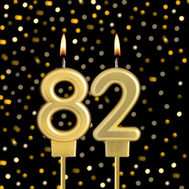 82 numaralı doğum günü mumu bulanık ışıklarla siyah arka planda.
