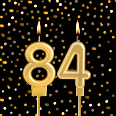 84 numaralı doğum günü mumu, bulanık ışıklarla siyah arka planda.