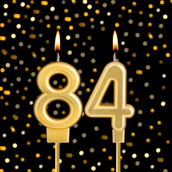 84 numaralı doğum günü mumu, bulanık ışıklarla siyah arka planda.