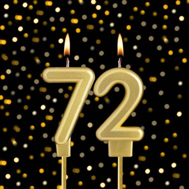 72 numaralı doğum günü mumu bulanık ışıklarla siyah arka planda.