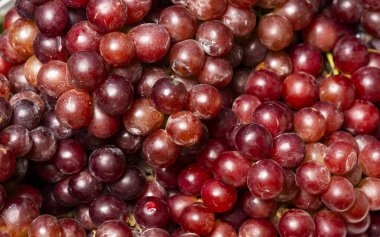 Yerel bir pazarda canlı renklerle ve doğal dokularla sergilenen taze kırmızı üzümler..