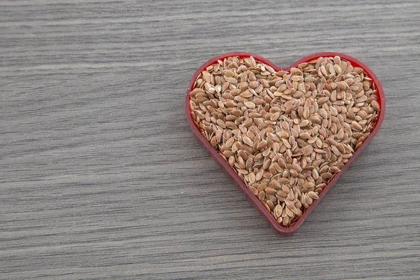 Diet hälso-och hälsosam mat. RAW linfrön Linoljefärg hjärtformade på träplatta bakgrund. — Stockfoto