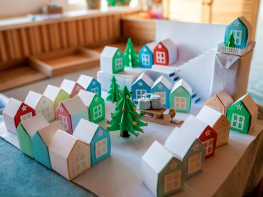 Origami takvimi, Noel köyü, kağıt işleri. Şirin bir kız, içinde sayılar ve kağıt yeşili ağaçlar olan küçük kağıt evlere bakıyor, çocuklarla mevsimsel aktiviteler, kapalı bir yaşam tarzı.
