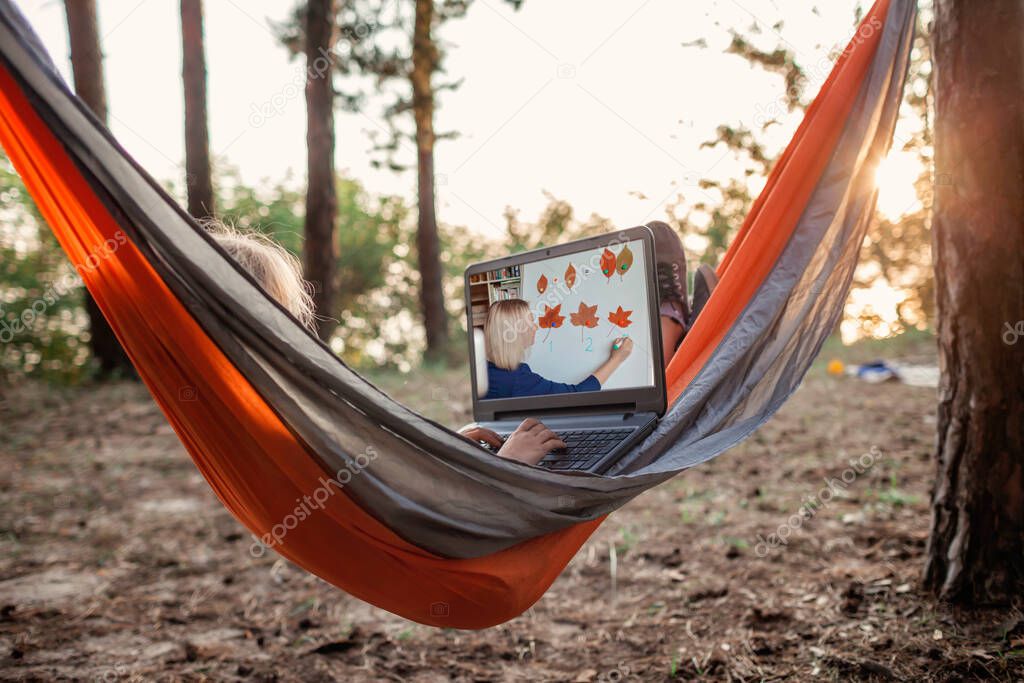 Cute kid using digital gadget for reading and learning in hammock in the wild forest, online education, new normal and social distance lifestyle, focus on keyboard