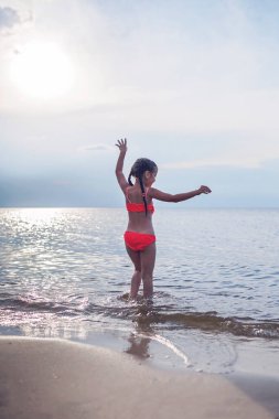 Gün batımında denize koşan tatlı küçük kız, bir sürü sıçrama ve mutluluk, yaz yaşam tarzı.