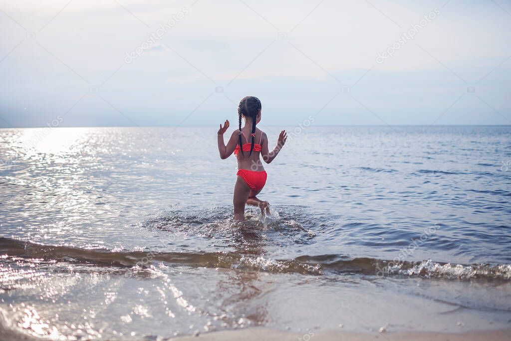 Cute little girl running into the sea in sunset light, lots of splashes and happiness, summer lifestyle