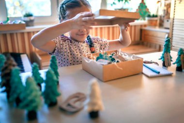 Şirin bir kız Noel için ailelere Noel hediyesi hazırlıyor ve onlara etiket imzalıyor. Küçük bir çam ağacı, etiket ve bayram kutuları gibi yeşil bir koni. El yapımı hediyeler, sıfır atık tatil.