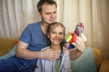 İnternetten alışveriş konsepti. Güzel kızıyla yakışıklı bir baba akıllı telefonuyla eğleniyor örgü şapka takıyor ve küçük alışveriş torbalarıyla evde alışveriş yapıyorlar, Kara Cuma ve satış.