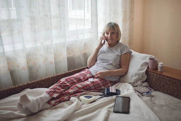 Old woman in bed looking at screen of laptop and consulting with a doctor online at home, telehealth services during lockdown, distant video call, modern tech healthcare application