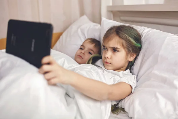 Dois irmãos assistindo vídeo em dispositivo eletrônico móvel na cama, vício em gadgets, estilo de vida — Fotografia de Stock