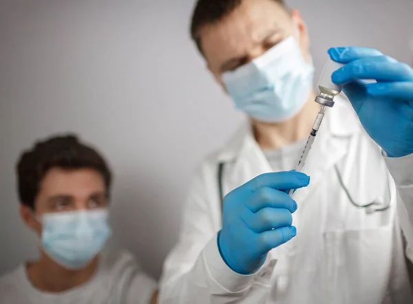 Врач в медицинской маске и перчатках держит ампулу и шприц с коронавирусной вакциной, простудой и гриппом — стоковое фото