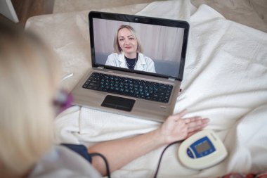 Yatakta yaşlı bir kadın dizüstü bilgisayara bakıyor ve evdeki bir doktora danışıyor.