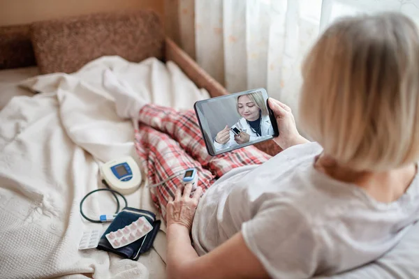 Yatakta yaşlı bir kadın dizüstü bilgisayara bakıyor ve evdeki bir doktora danışıyor.