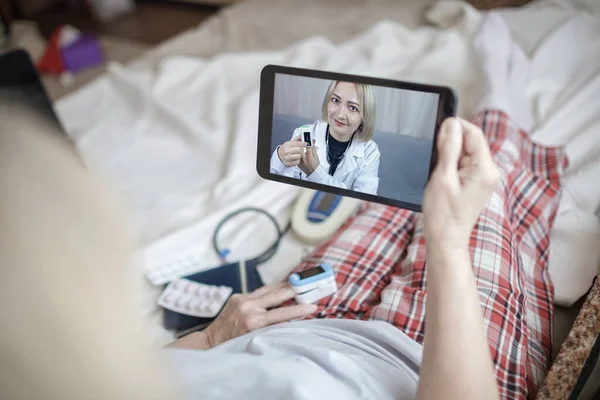Старуха в постели смотрит на экран ноутбука и консультируется с врачом онлайн на дому, телездоровье — стоковое фото