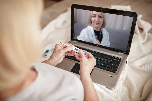침대에 있는 할머니는 노트북 화면을 보고 집에 있는 의사와 상담을 합니다. 텔레 건강이죠. — 스톡 사진