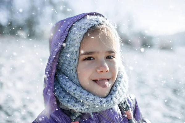 Menina em chapéu de malha desfrutando primeira neve de inverno e degustação com língua, estilo de vida ao ar livre — Fotografia de Stock