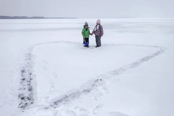 Chłopiec i dziewczyna bawią się i usuwając śnieg z lodu na zamarzniętym jeziorze w kształcie serca — Zdjęcie stockowe