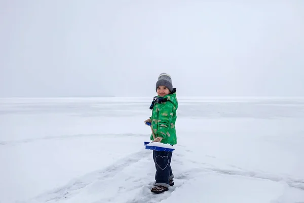 Ragazzo rimozione della neve dal ghiaccio sul lago ghiacciato, inverno, silenzio e natura selvaggia, stile di vita — Foto Stock