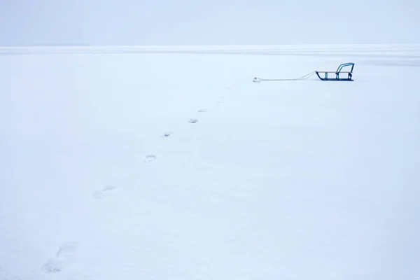 Paesaggio invernale con percorso piedi e slitta solitaria sul lago ghiacciato ghiacciato, sfondo — Foto Stock