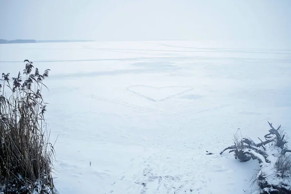 Heart shape feet path in the snow on frozen lake. Winter romantic, icy landscape