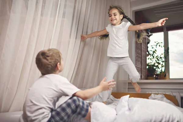 Crianças de pijama pulando na cama no quarto, dormindo saudável — Fotografia de Stock